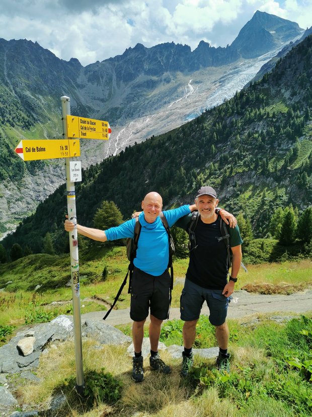Stefan und Manno stehen an einem Wegweiser vor Bergpanorama
